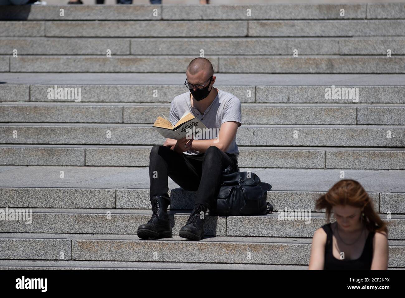 Un homme lit le livre « Pourquoi je ne parle plus à White People About Race » sur les marches de Trafalgar Square, Londres Banque D'Images