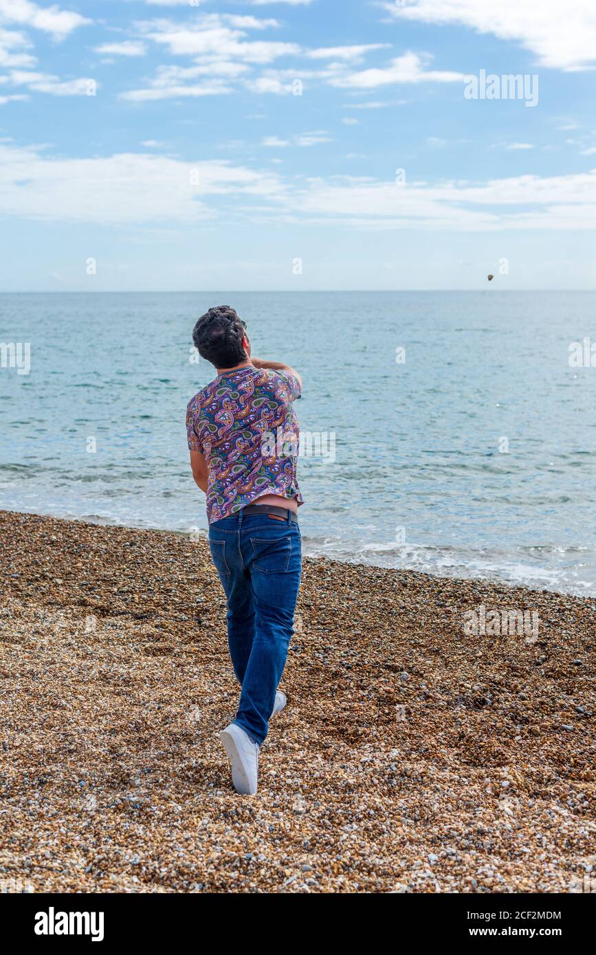 Homme jetant une pierre dans la mer sur un cailloux plage Banque D'Images