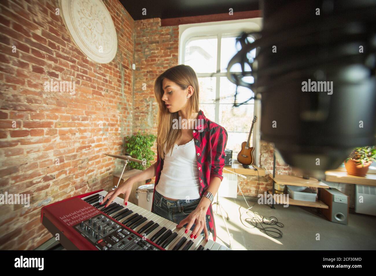 Un jeu inspiré et attentif. Belle femme enregistrant de la musique,  chantant et jouant du piano tout en étant debout dans le loft ou à la  maison. Concept de passe-temps, musique, art