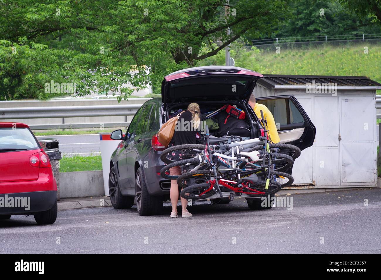 Un couple marié dans un parking se trouve à côté d'une voiture pleine de matériel de voyage. Banque D'Images