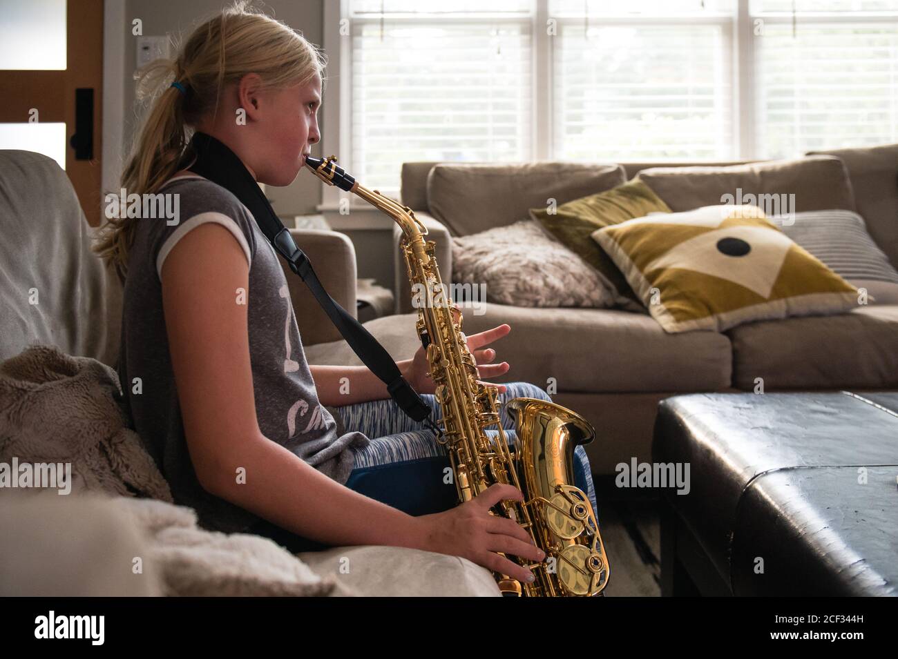Jeune fille à queue de cheval blonde jouant le saxophone alto un salon Banque D'Images