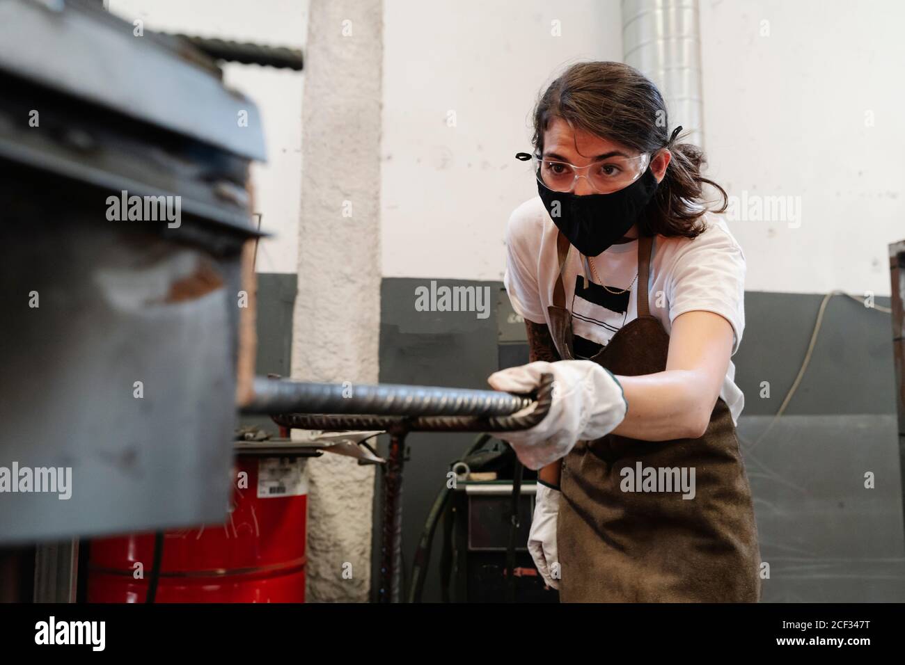 Forgeron féminin sérieux dans un masque de protection et des gants en atelier travail de métal Banque D'Images