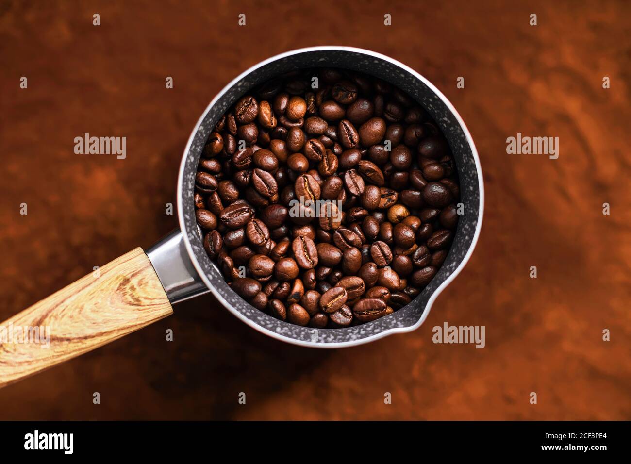 Vue de dessus de la cezve avec une poignée en bois dans laquelle sont torréfiés les grains de café naturels, et la cezve se tient sur la surface du café moulu. Banque D'Images