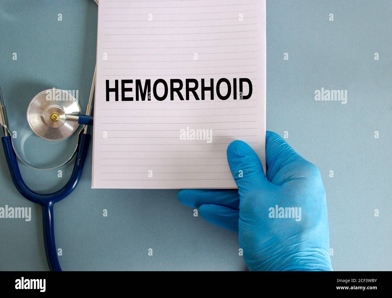 Main dans un gant bleu, carte blanche avec le mot « hémorroïde » et stéthoscope. Magnifique fond bleu. Concept médical. Banque D'Images
