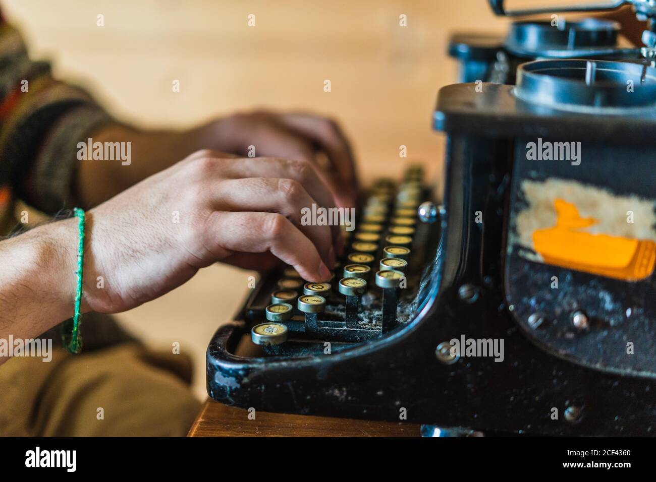 Vue latérale rognée des mains d'un homme anonyme en chandail dactylographie sur une machine à écrire rétro sur une table en bois à la maison Îles Féroé Banque D'Images