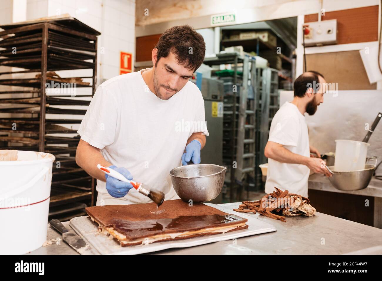 Pâtisserie concentrée faire cuire l'étalement de la garniture de chocolat sur un gâteau savoureux pendant debout près de la table dans la boulangerie Banque D'Images