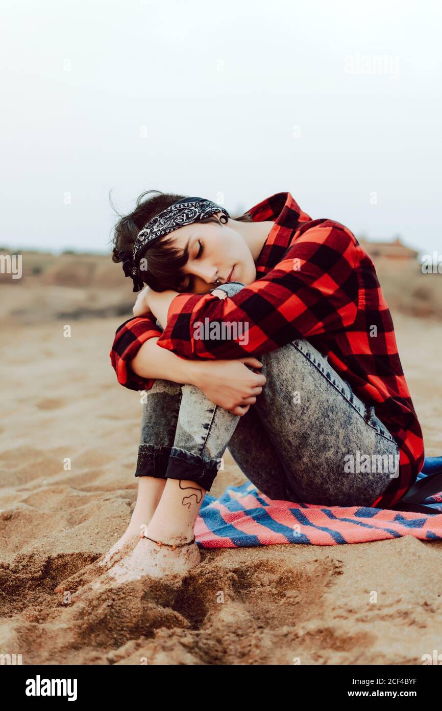 Une femme hipster pensive assise sur une plage de sable Banque D'Images