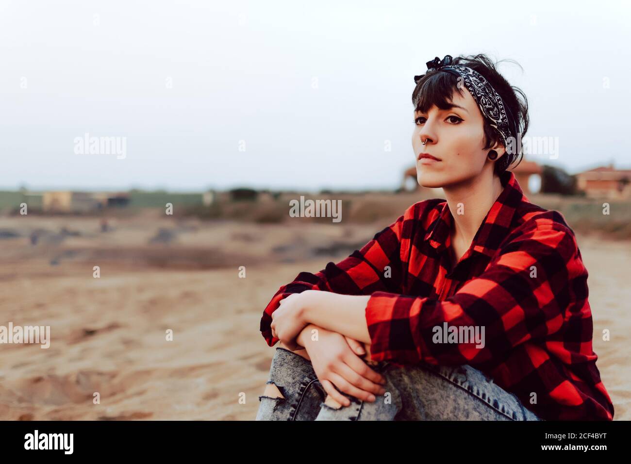 Une femme hipster pensive assise sur une plage de sable Banque D'Images
