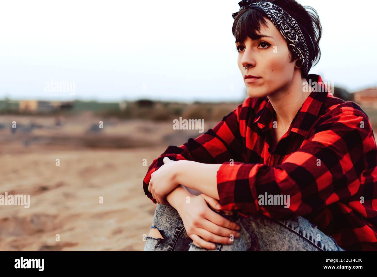 Une femme hipster pensive assise sur une plage de sable Banque D'Images