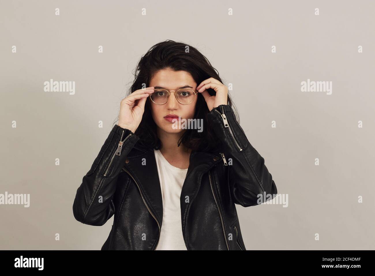 Femme élégante et bien pensée aux cheveux foncés dans une veste de motard noire et regardant l'appareil photo sur fond gris en studio Banque D'Images