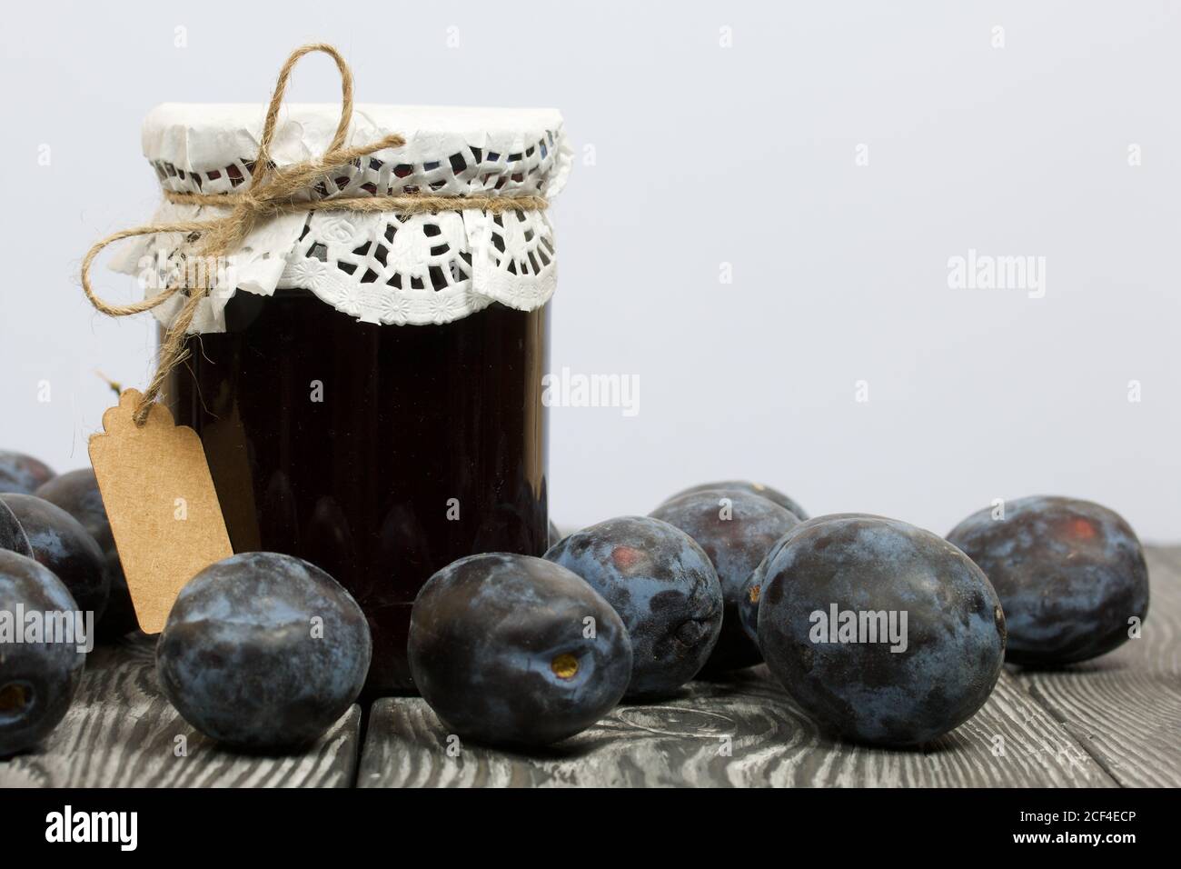 Pot de confiture de prune. Avec une étiquette d'inscription. Des prunes sont dispersées à proximité. Sur des planches de pin peintes. Banque D'Images