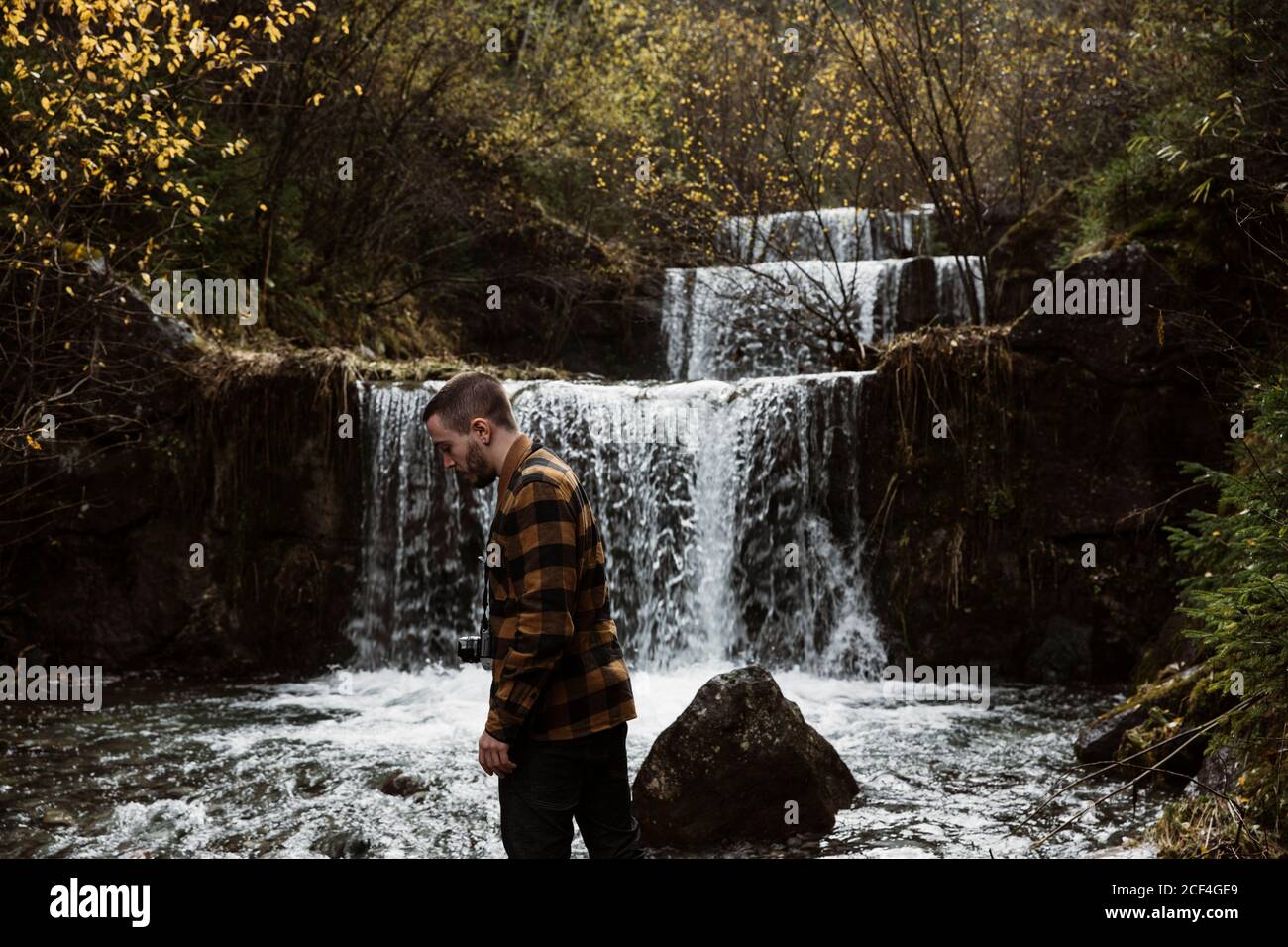 Vue latérale de l'homme avec caméra accrochée autour du cou en cascade naturelle dans la forêt Banque D'Images