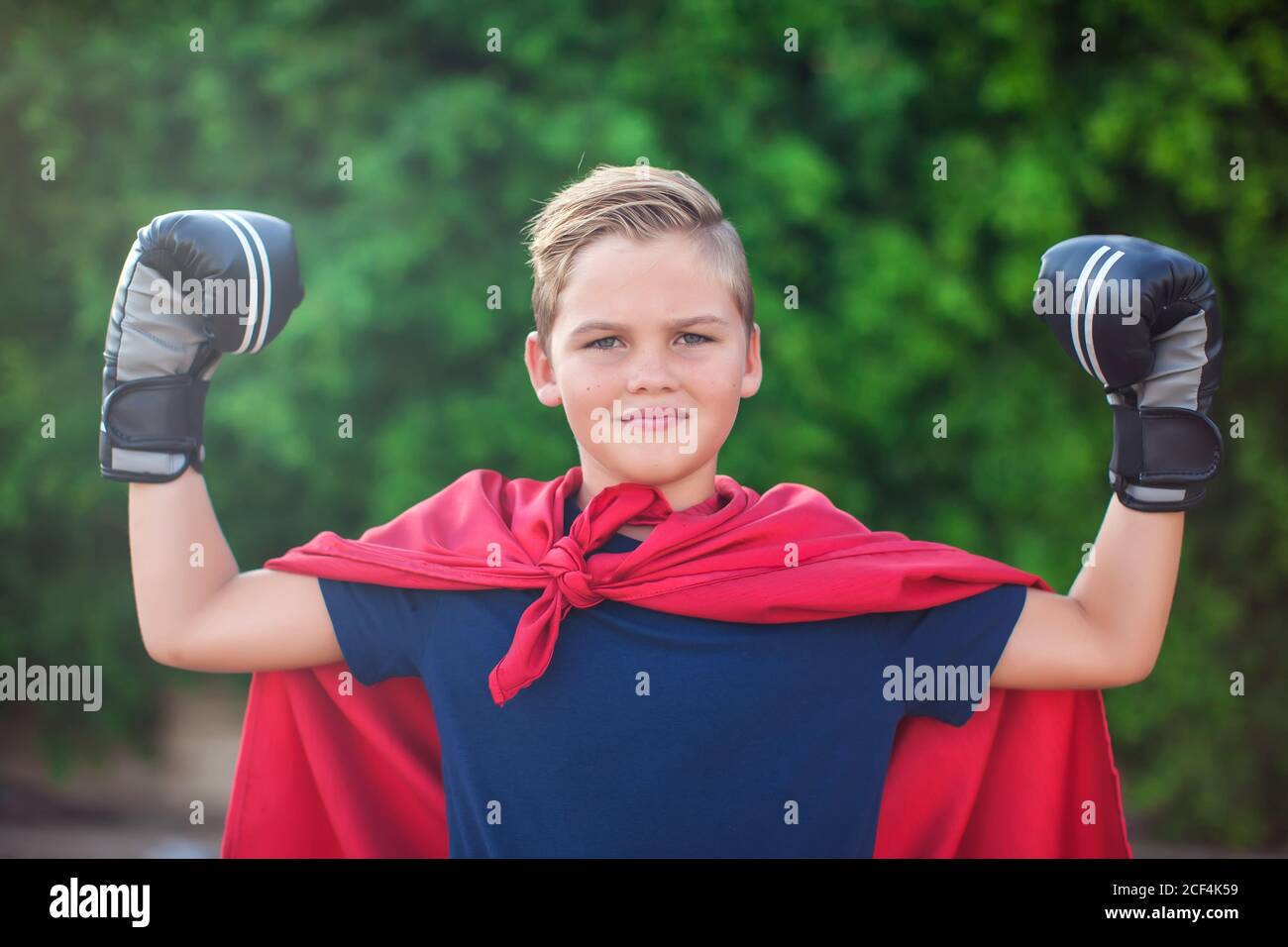 Super-héros de garçon avec des gants de boxe et un manteau rouge montrant de la puissance en extérieur. Concept d'enfance, de réussite et de liberté Banque D'Images