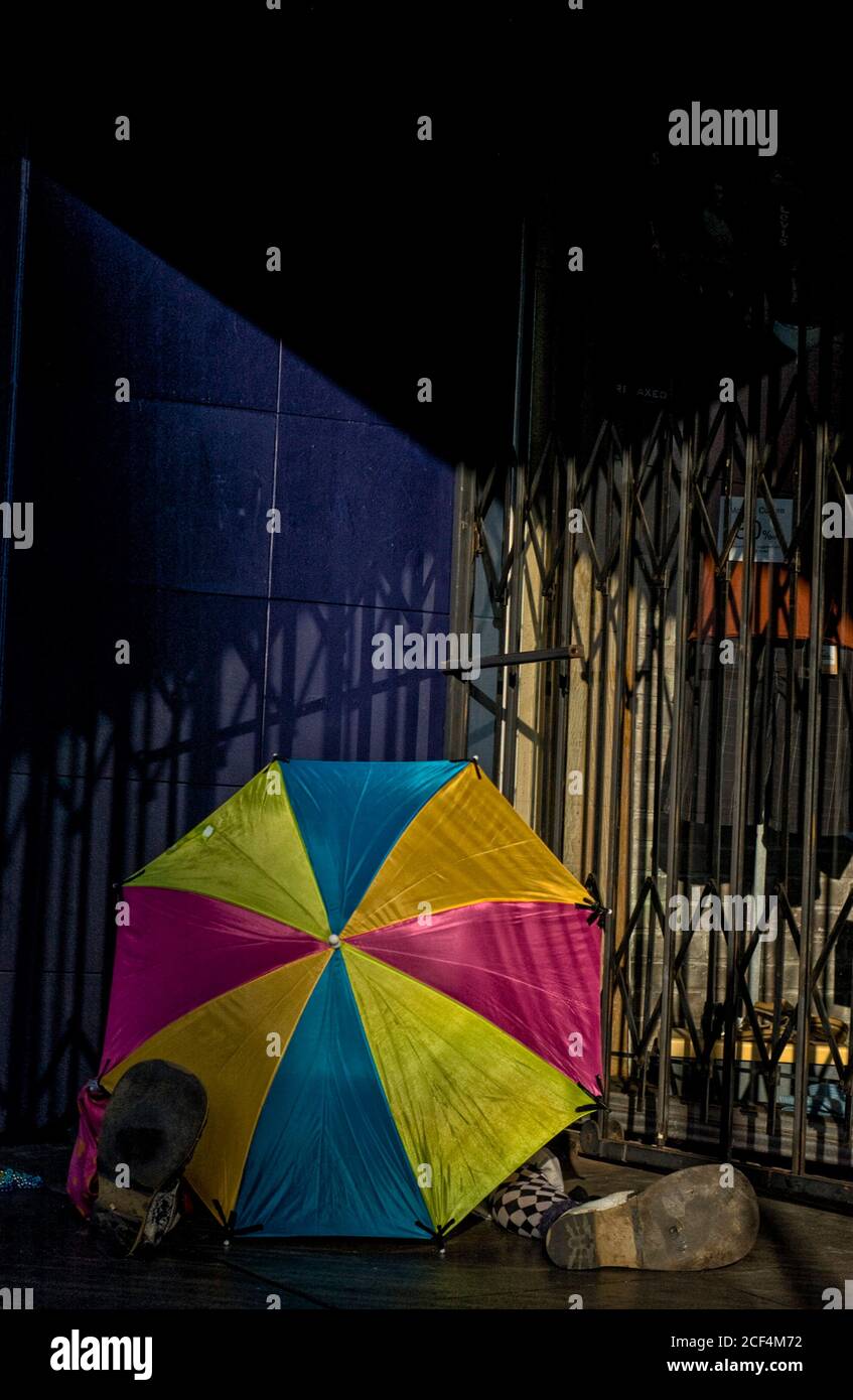 Un clown se protège du soleil avec un parapluie coloré. Banque D'Images