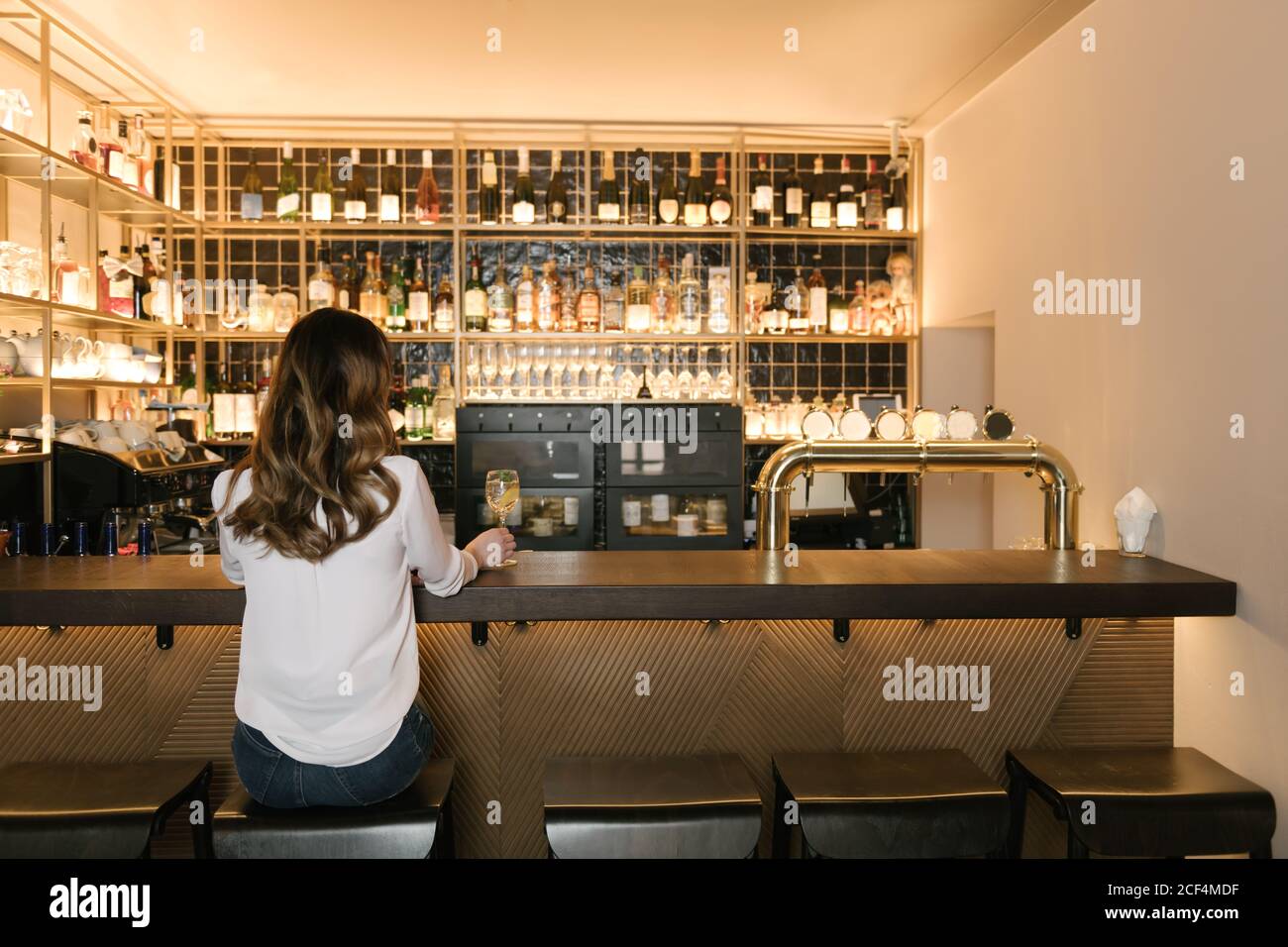 De l'arrière-plan de la femme anonyme tenant un cocktail tout en s'asseyant au bar d'un restaurant confortable Banque D'Images