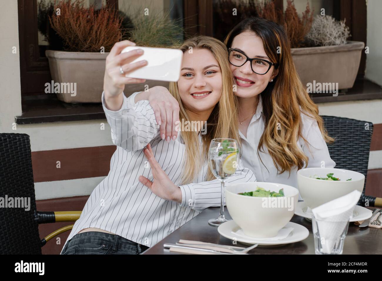 Deux amies élégantes souriant et posant pour le selfie asseyez-vous à table dans un restaurant confortable Banque D'Images