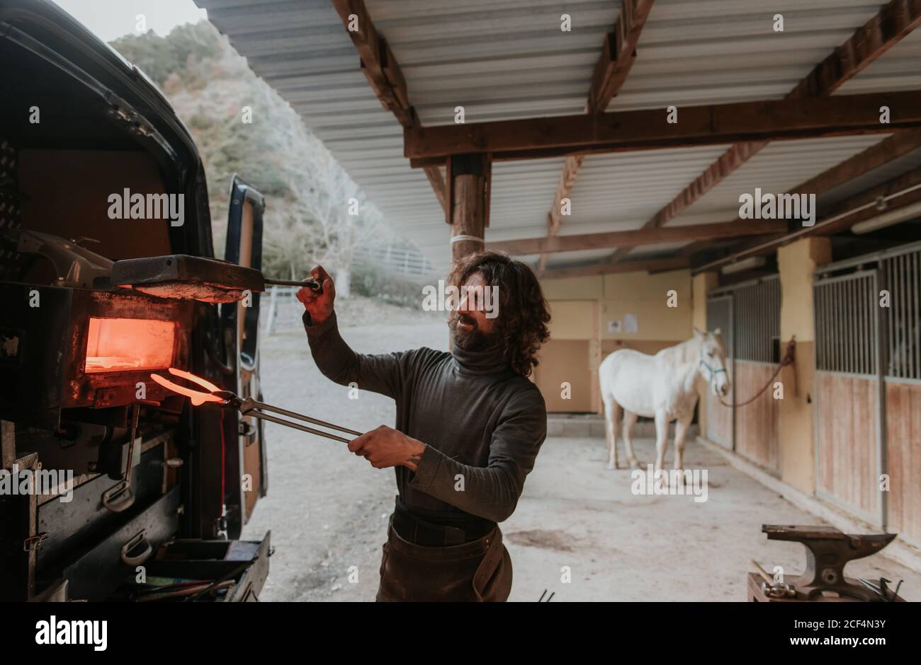 Un adulte porteur qui prend le fer à cheval du four portable arrière de la voiture tout en travaillant près de stable sur le ranch Banque D'Images