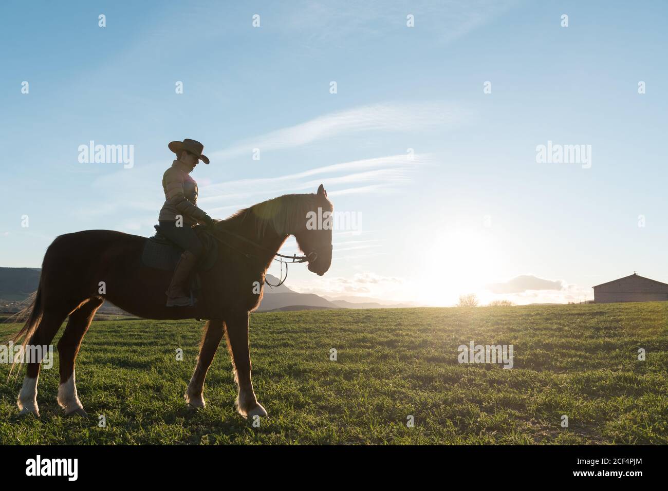 Femme à cheval contre le coucher du soleil sur le ranch Banque D'Images