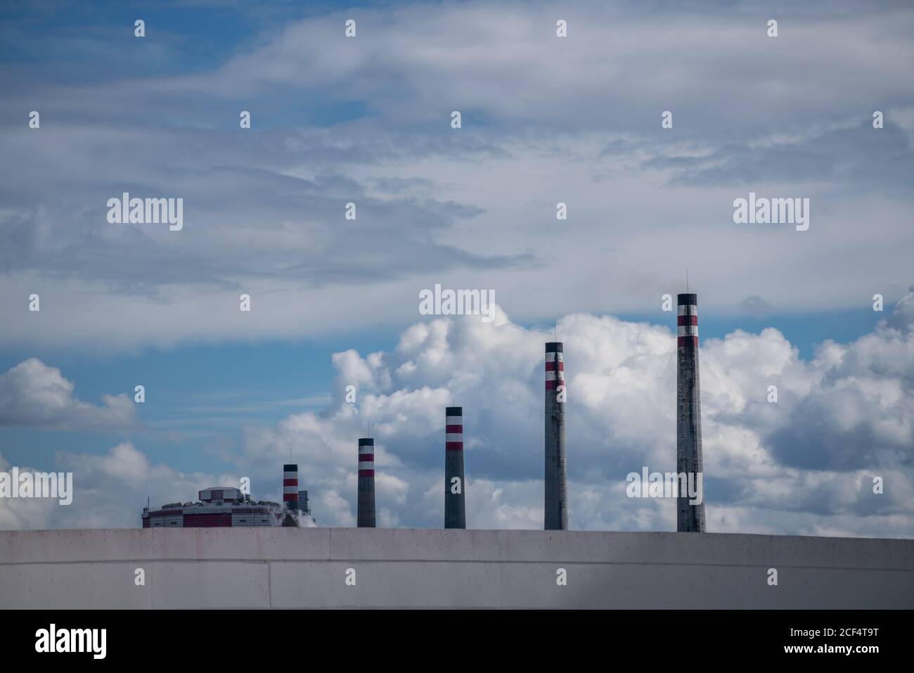 Cheminées d'échappement industrielles en rangée derrière le mur gris sur l'arrière-plan de ciel pittoresque nuageux Banque D'Images