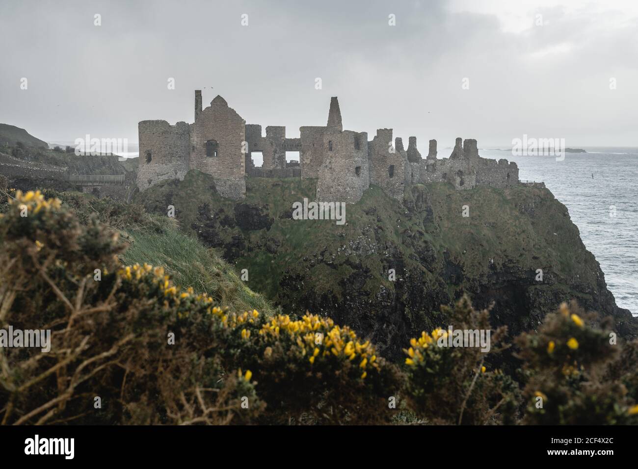 Paysage majestueux avec des ruines de l'ancienne pierre Dunluce Castle in lumière du soleil située au bord de la falaise avec l'arc-en-ciel qui se brise ciel orageux et vagues de mer battant contre le rivage Banque D'Images