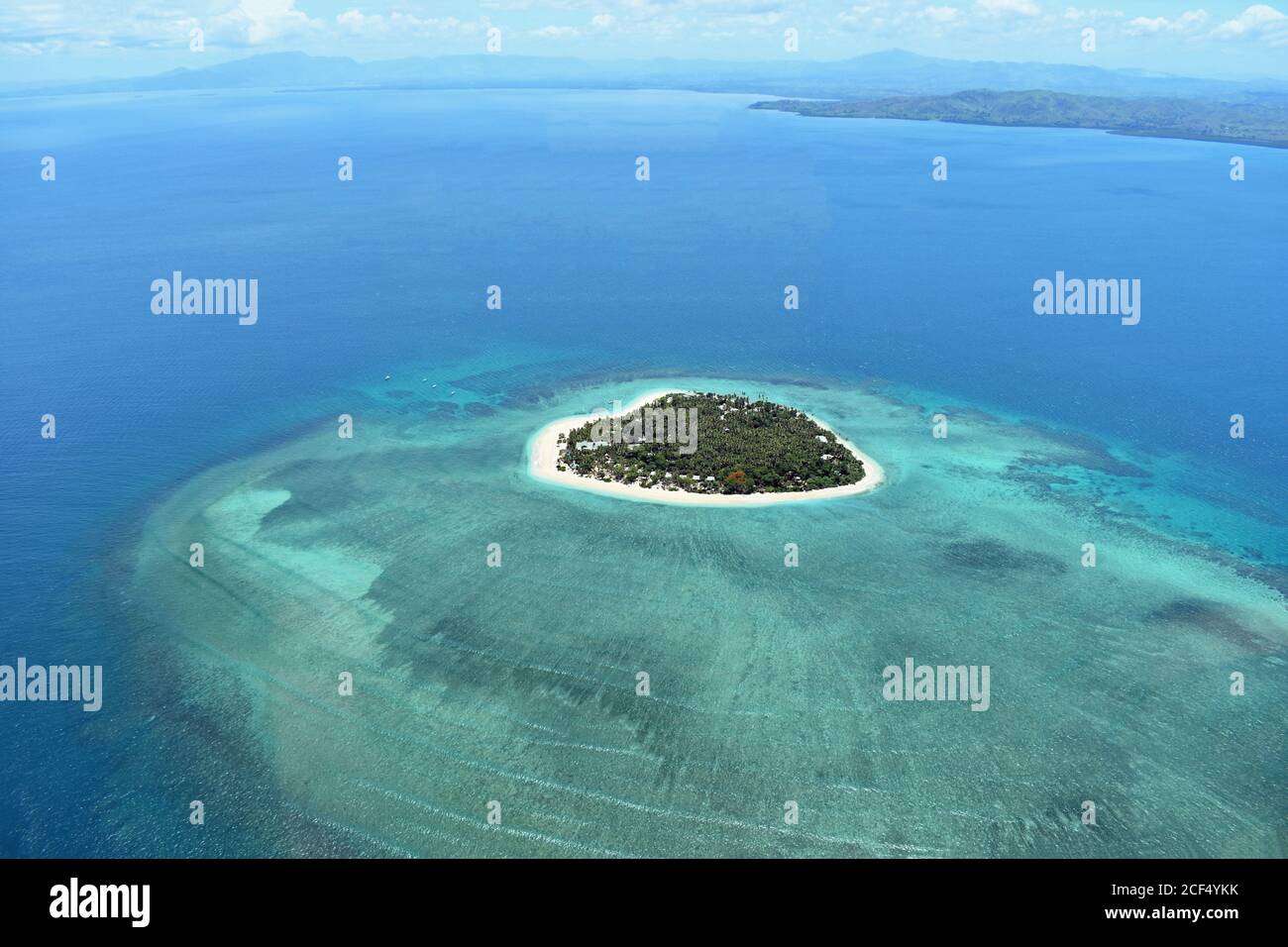 L'île de Tavarua au large de la côte de Viti Levu, Fidji. Une île en forme de coeur dans le Pacifique sud entourée par un récif de corail. Le continent est au loin Banque D'Images