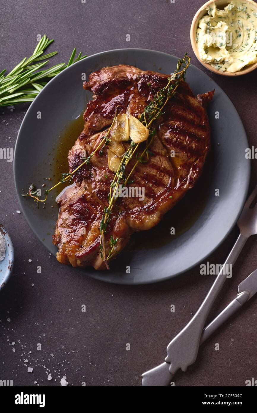 Steak de bœuf Angus de choix cuit à la ribeye, noir, au beurre, au sel de mer, aux herbes et aux tranches d'ail. Banque D'Images