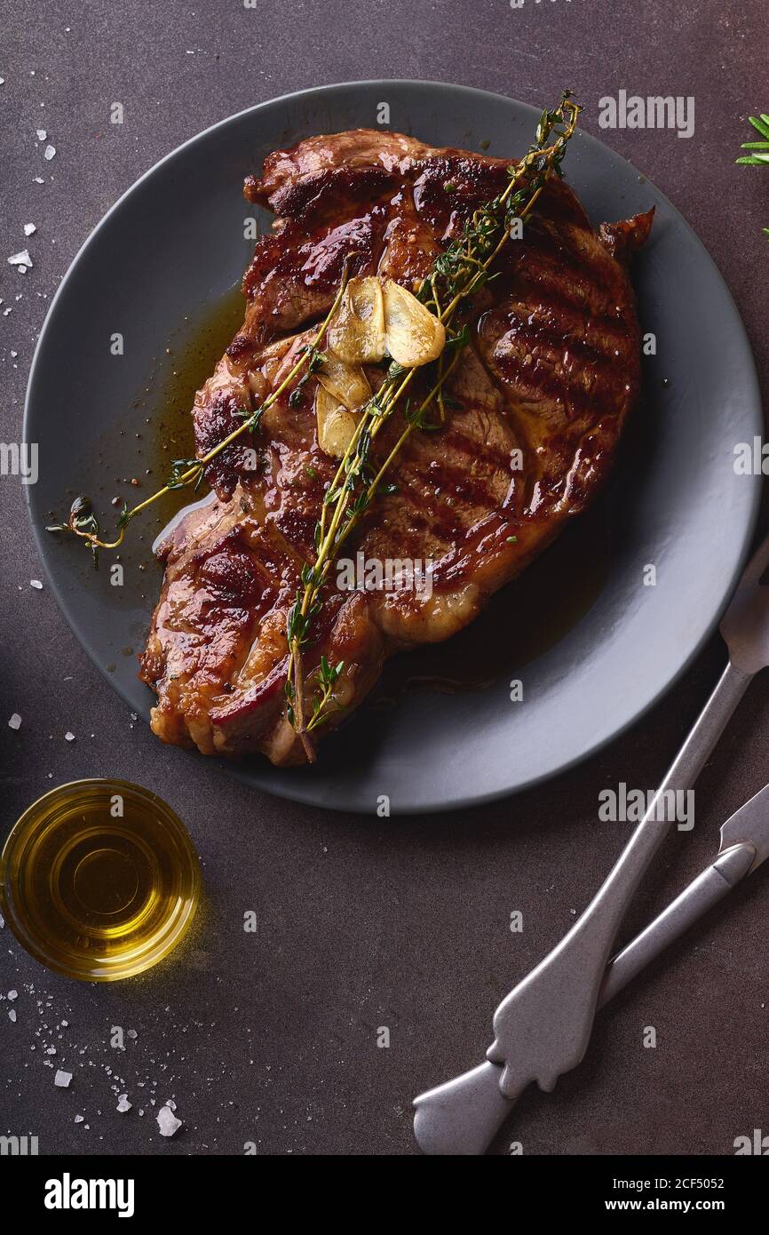 Steak de bœuf Angus de choix cuit à la ribeye, noir, au beurre, au sel de mer, aux herbes et aux tranches d'ail. Banque D'Images