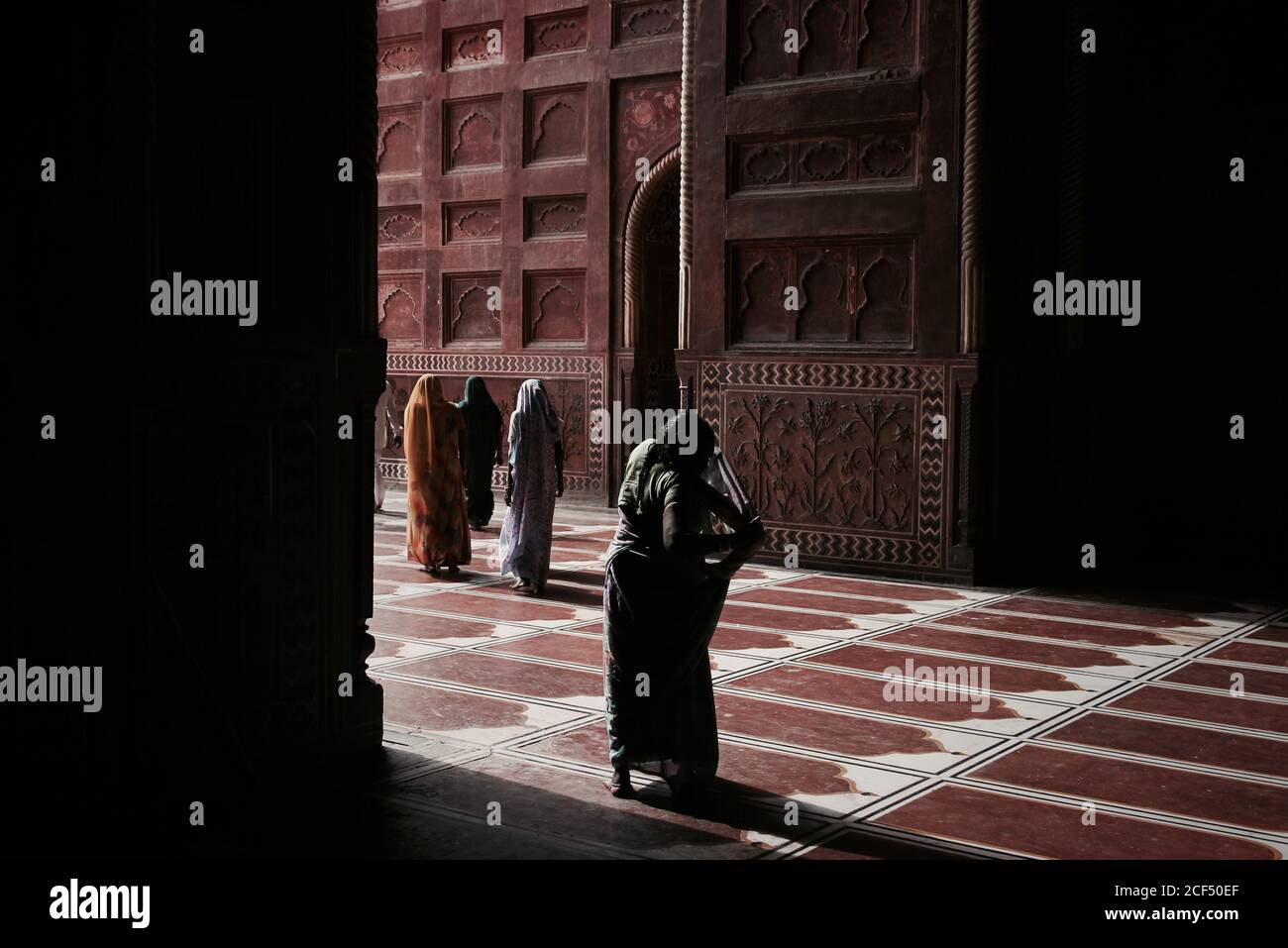 Vue arrière de femmes méconnaissables portant le hijab traditionnel entrant dans l'ancienne mosquée avec sol et murs ornementaux Banque D'Images