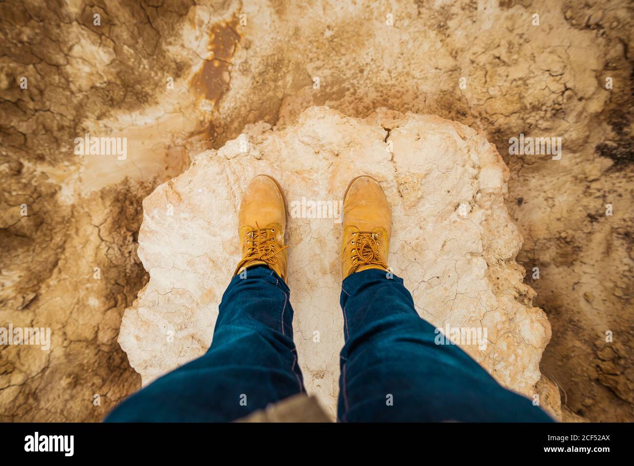 D'en haut de la vue de la personne anonyme jambes en bottes brunes et jeans bleus se tenant sur la route de sable sale avec la montagne et le ciel sur un fond flou à Bardenas Reales, Navarre, Espagne Banque D'Images
