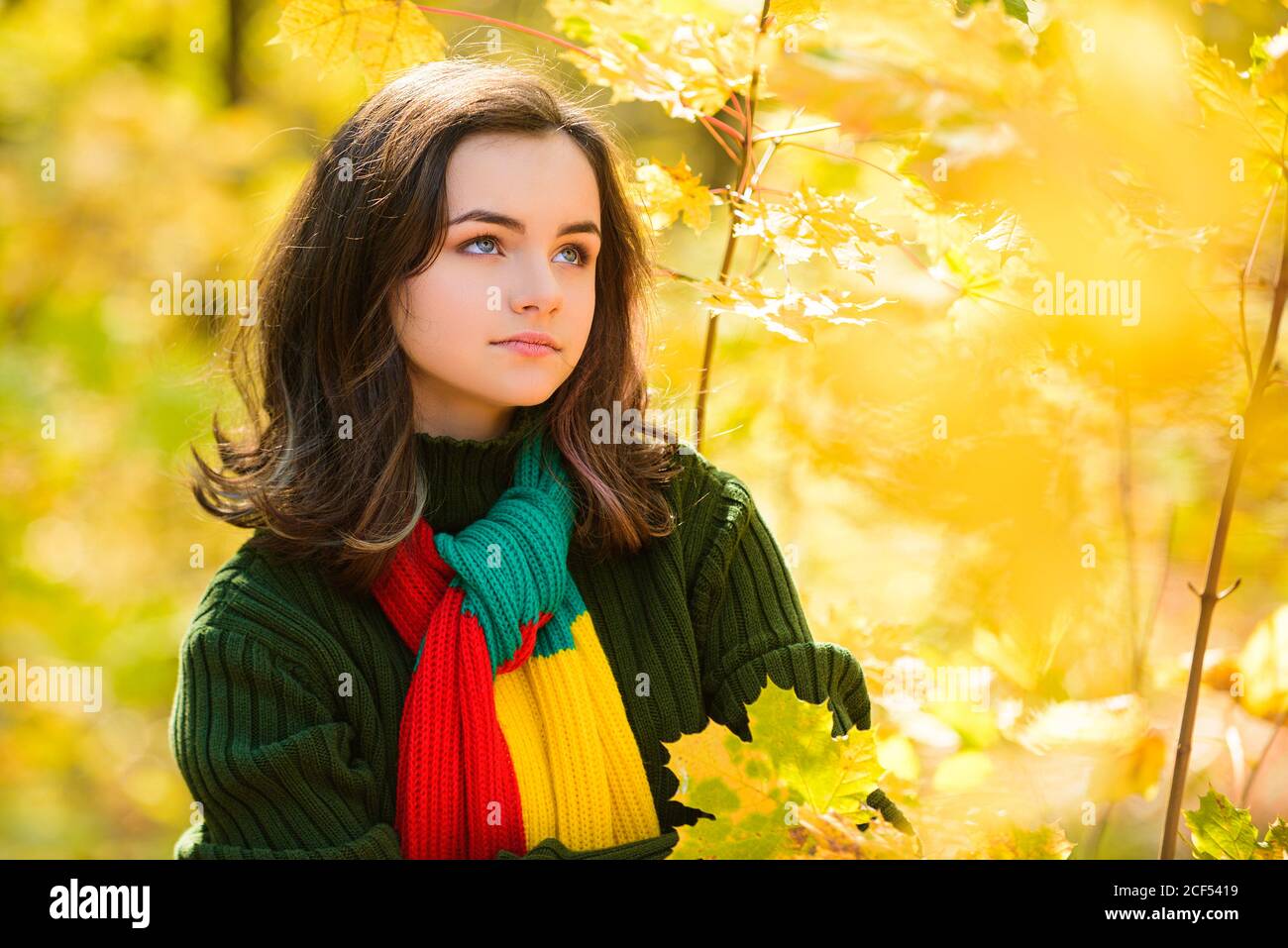 Adolescent d'automne. Portrait d'une jeune fille adolescente avec des feuilles d'automne devant le feuillage. Banque D'Images