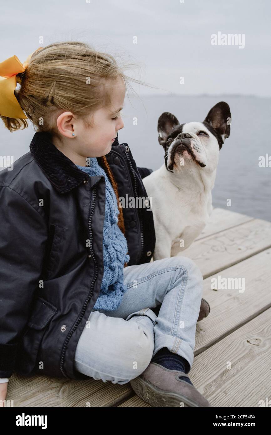 Petite fille avec un Bulldog français assis sur la jetée près de la mer par temps nuageux Banque D'Images