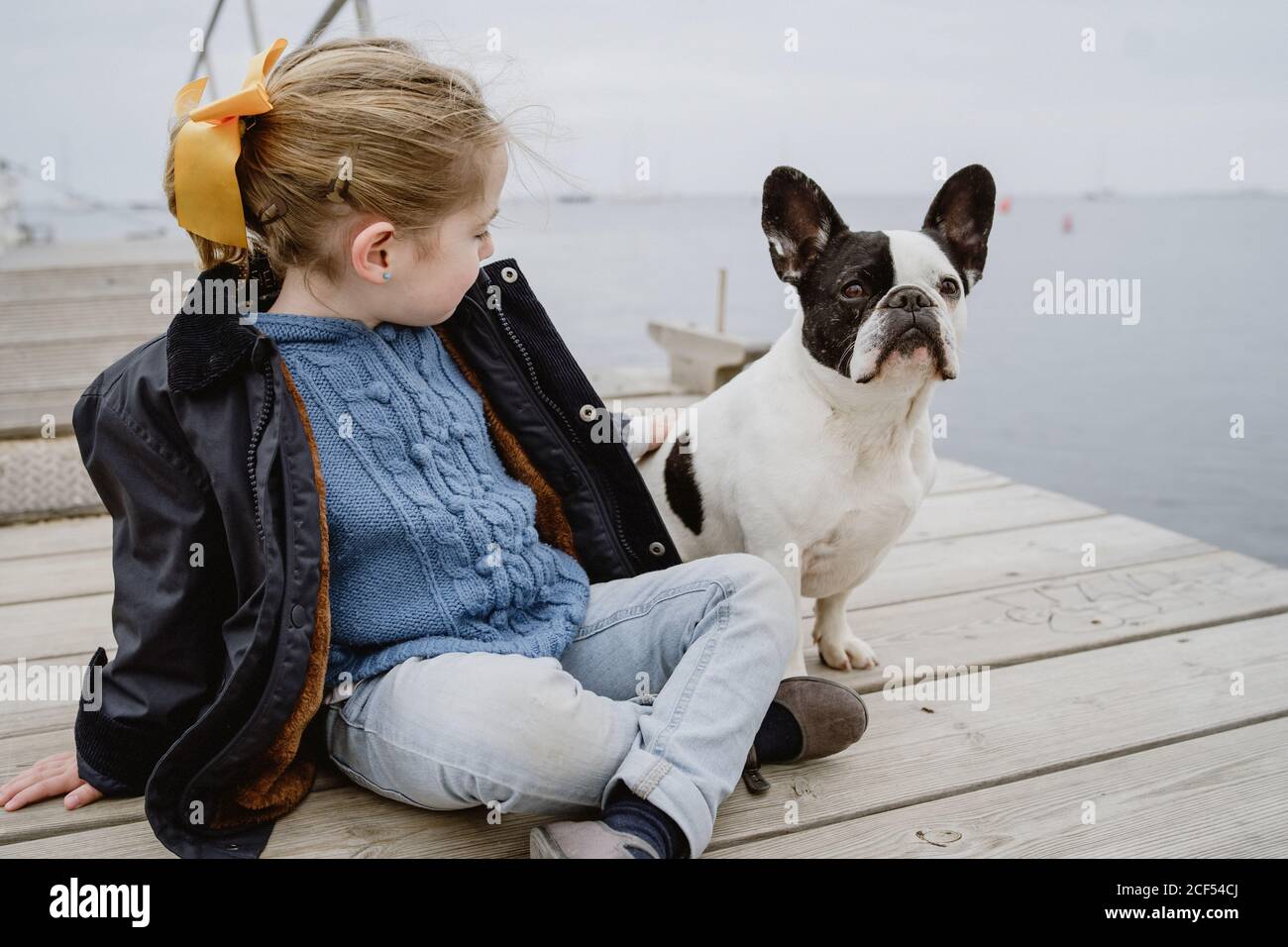 Petite fille avec un Bulldog français assis sur la jetée près de la mer par temps nuageux Banque D'Images