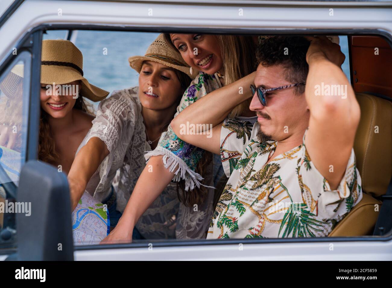 Des femmes animées et gaies dans un chapeau pointant sur la route sur la carte pendant que l'homme essaie de choisir la bonne façon dans la voiture dedans jour lumineux Banque D'Images