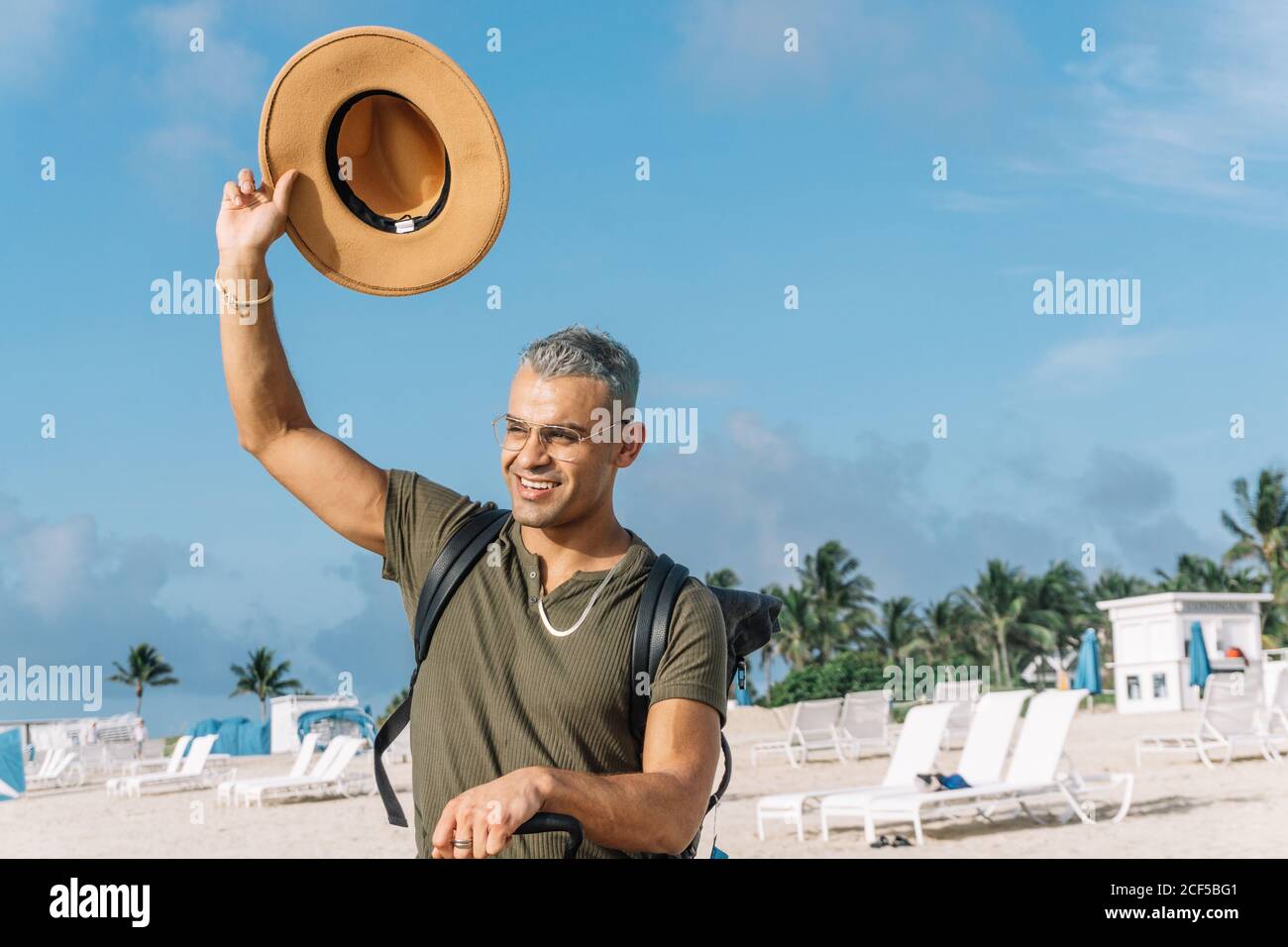 Jeune homme agitant avec son chapeau de cow-boy, assis sur ses bagages de transport. Concept de voyage Banque D'Images