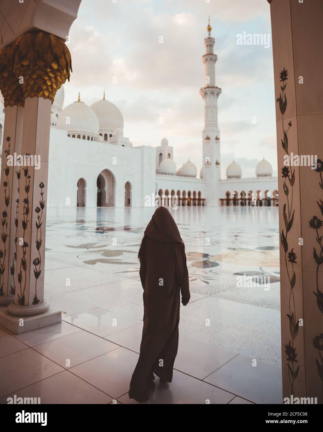 Vue arrière de la femme islamique anonyme en robe noire longue marchant sur la place carrelée de la majestueuse mosquée blanche, Dubaï Banque D'Images