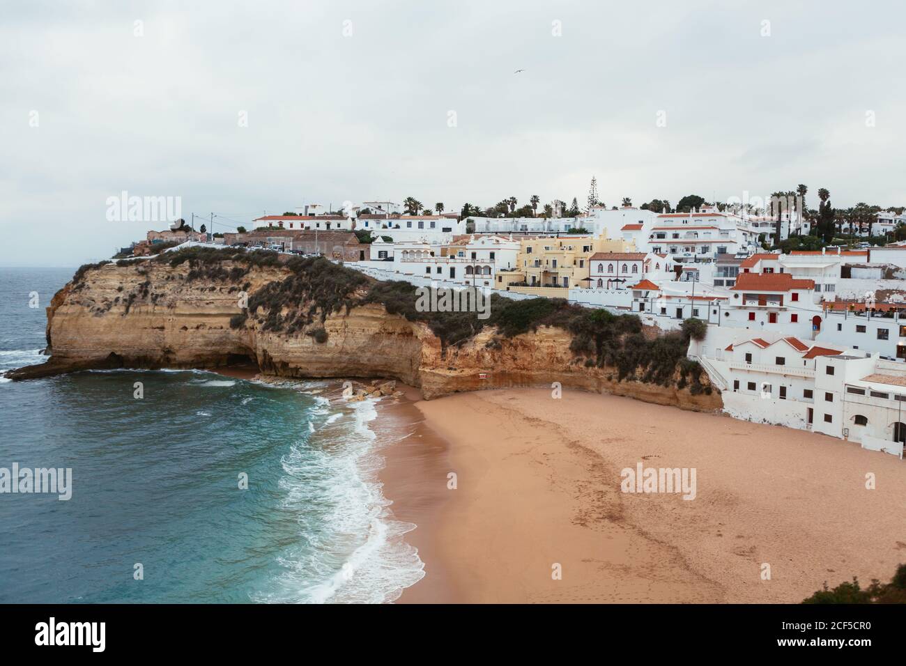 Mer orageux agitant près d'une falaise rugueuse et plage de sable avec Petite ville côtière le jour nuageux au Portugal Banque D'Images