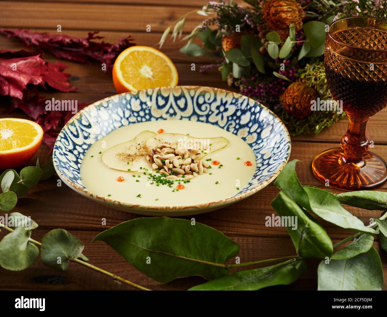 Bol de vichyssoise de poireaux fumé avec orange frais et verre de vin placé sur un plan d'examen en bois près des brindilles de diverses plantes Banque D'Images