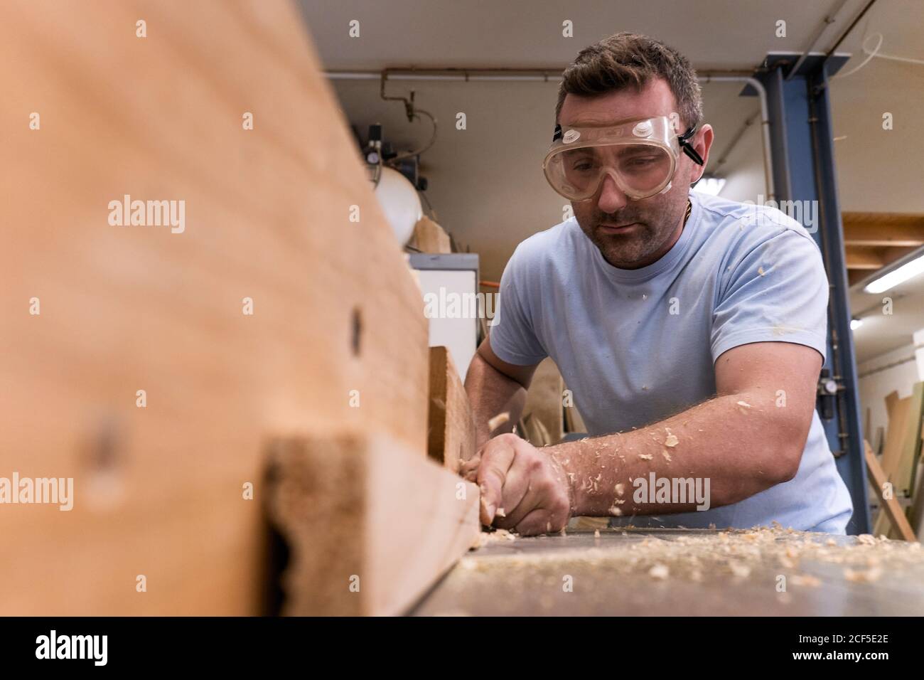 Faible angle de charpentier concentré dans les bois de fraisage de lunettes de protection tout en usant de détails à l'aide d'une machine électrique dans un atelier moderne et léger Banque D'Images
