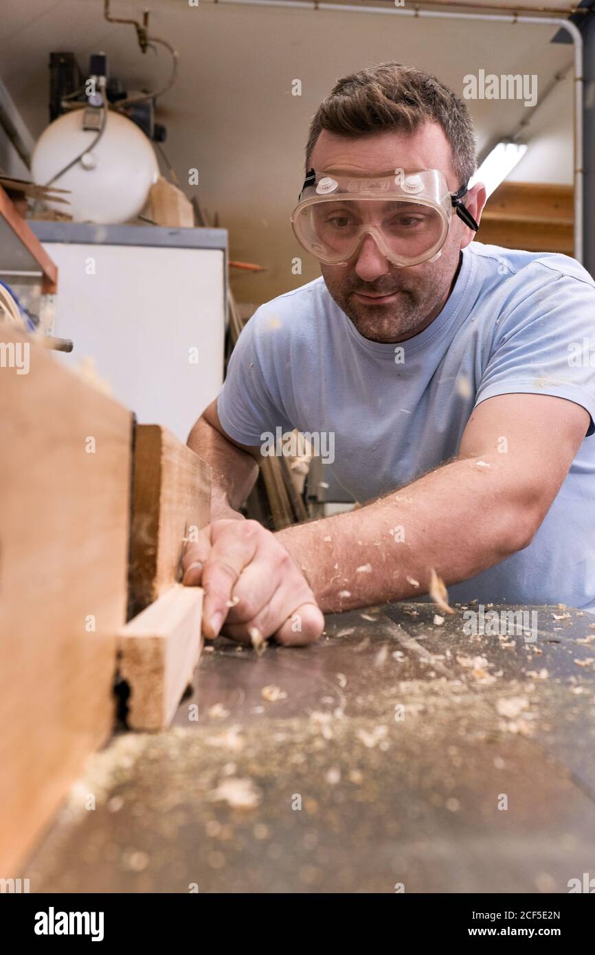 Faible angle de charpentier concentré dans les bois de fraisage de lunettes de protection tout en usant de détails à l'aide d'une machine électrique dans un atelier moderne et léger Banque D'Images