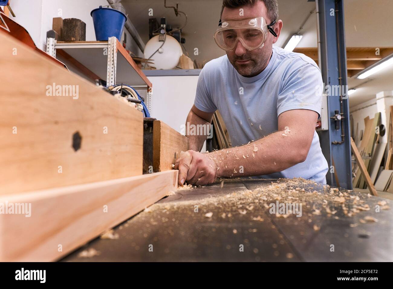 Faible angle de charpentier concentré dans les bois de fraisage de lunettes de protection tout en usant de détails à l'aide d'une machine électrique dans un atelier moderne et léger Banque D'Images