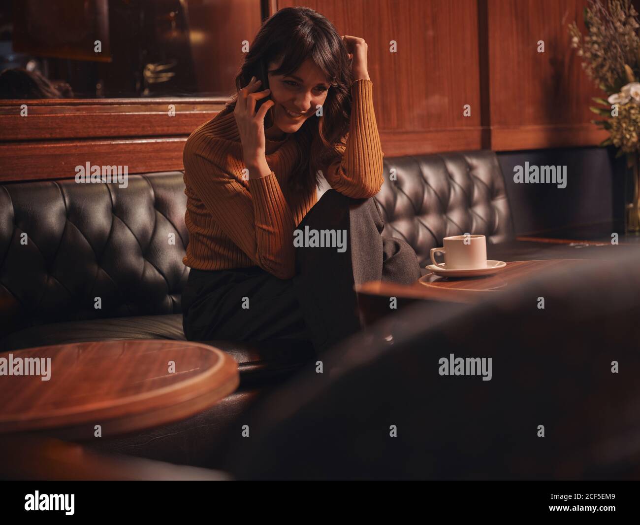 Femme élégante et gaie parlant sur un téléphone portable confortablement assis à une table ronde dans un café Banque D'Images