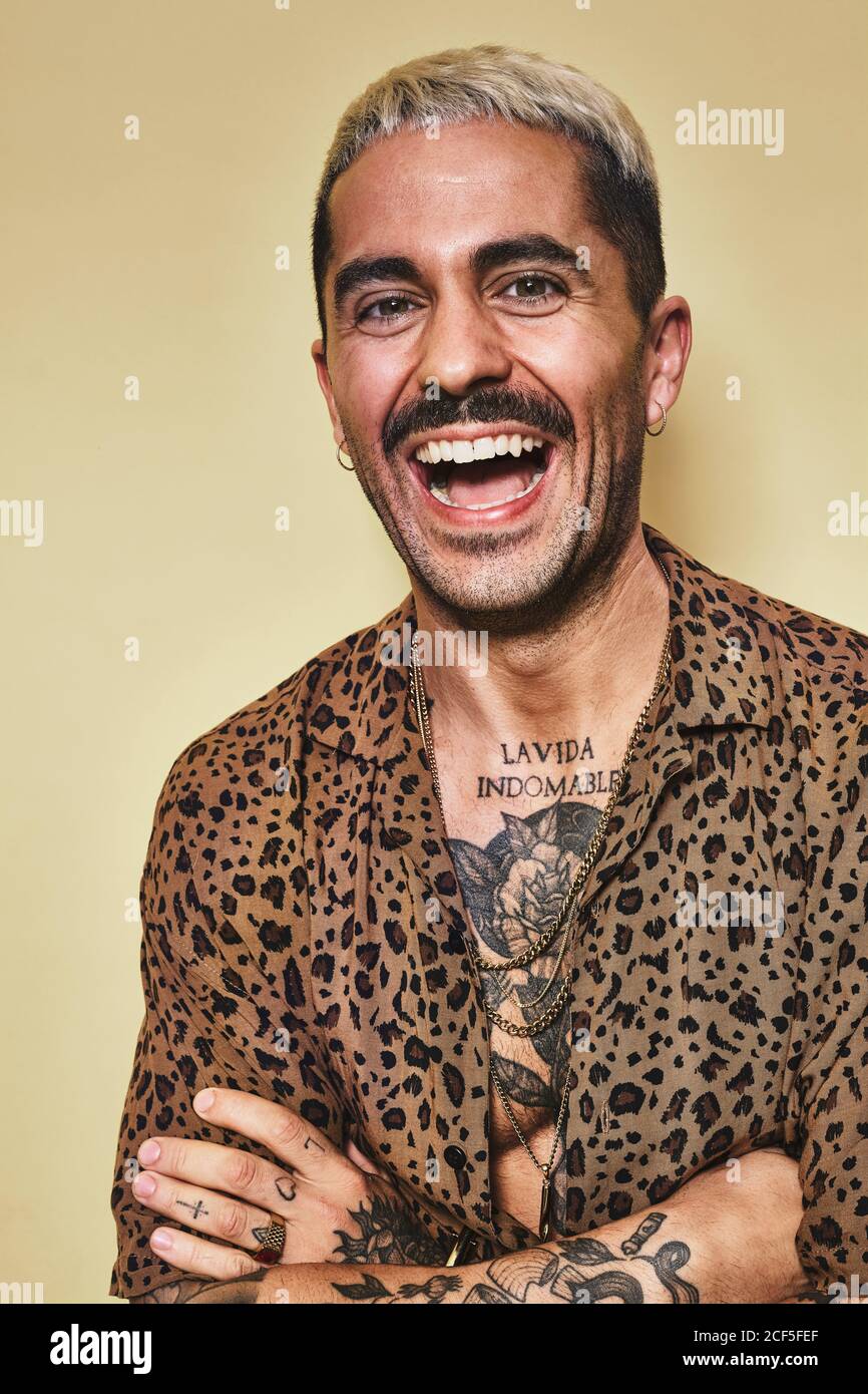 Portrait de modèle masculin tendance gai avec tatouages à la mode chemise leopard sur fond beige et regardant l'appareil photo Banque D'Images
