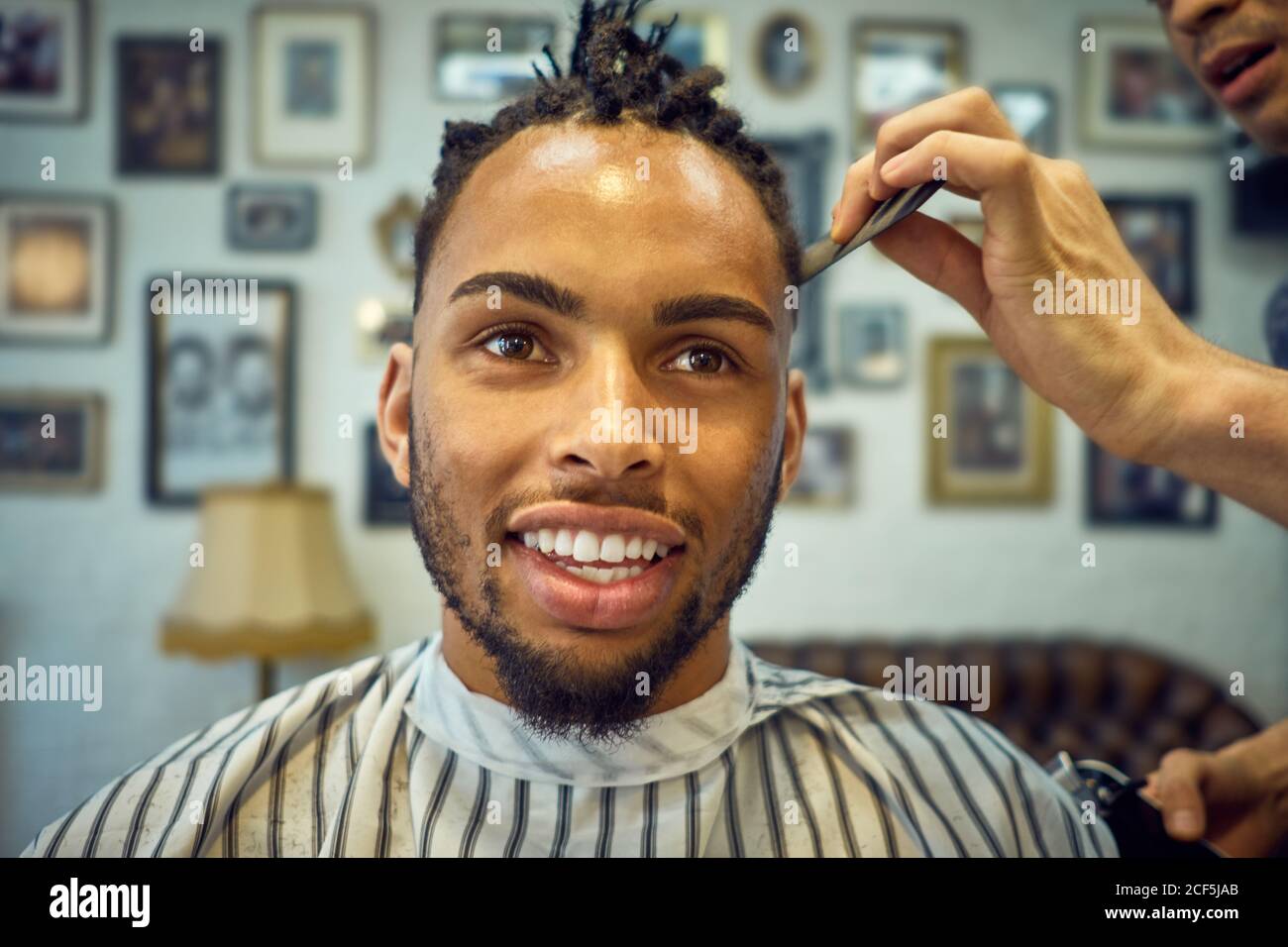 Rogner la vue de coiffeur anonyme faisant une coupe de cheveux moderne à un client afro-américain joyeux Banque D'Images