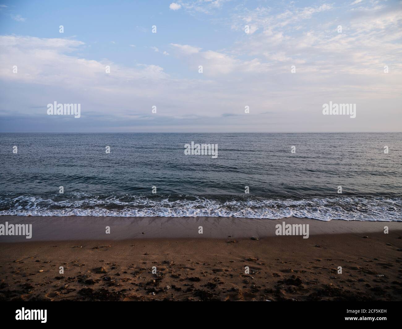 Plage de sable solitaire et océan calme avec vagues de mousse fond de ciel nuageux Banque D'Images