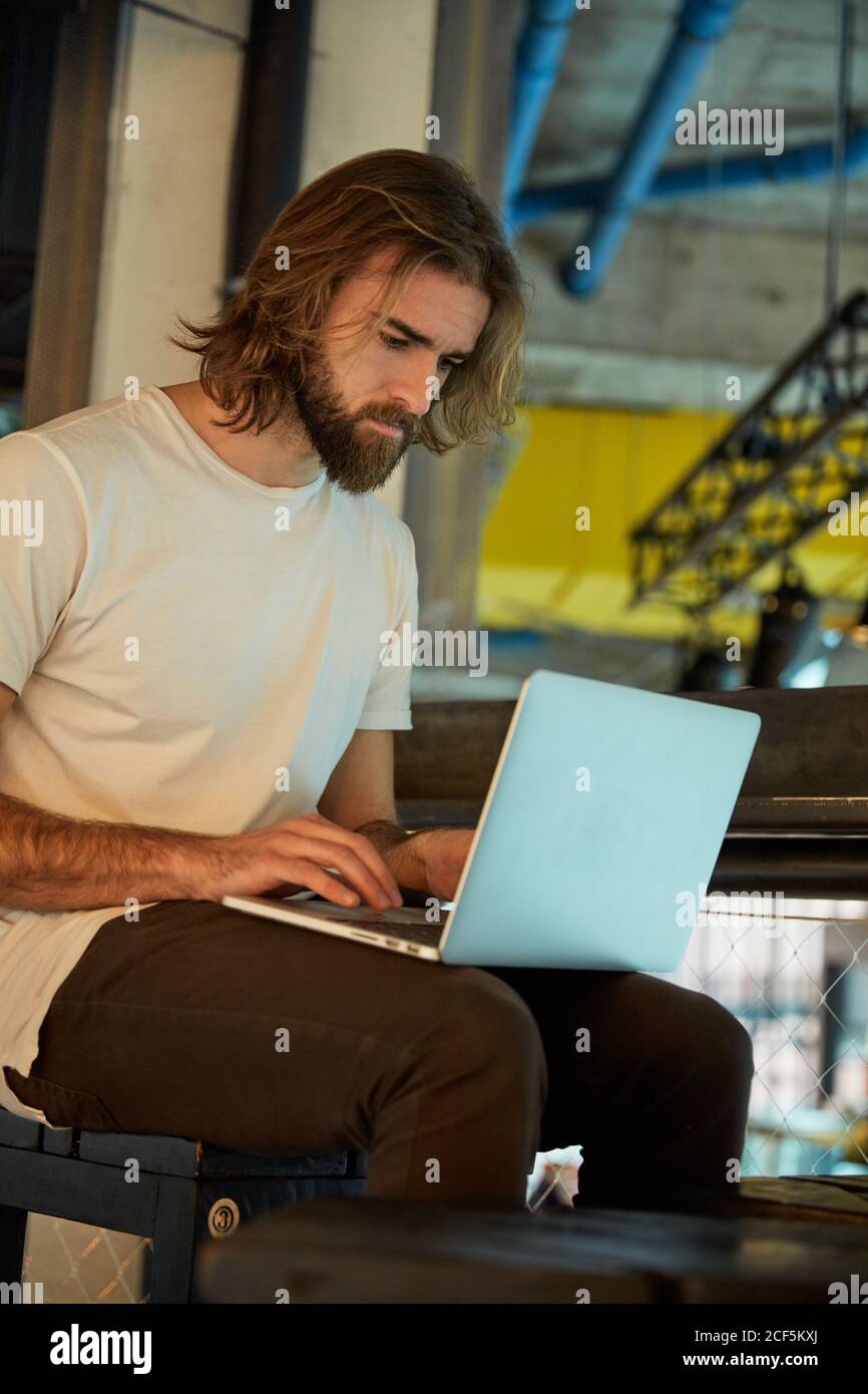 Jeune homme beau barbu assis et travaillant tenant le carnet tours Banque D'Images