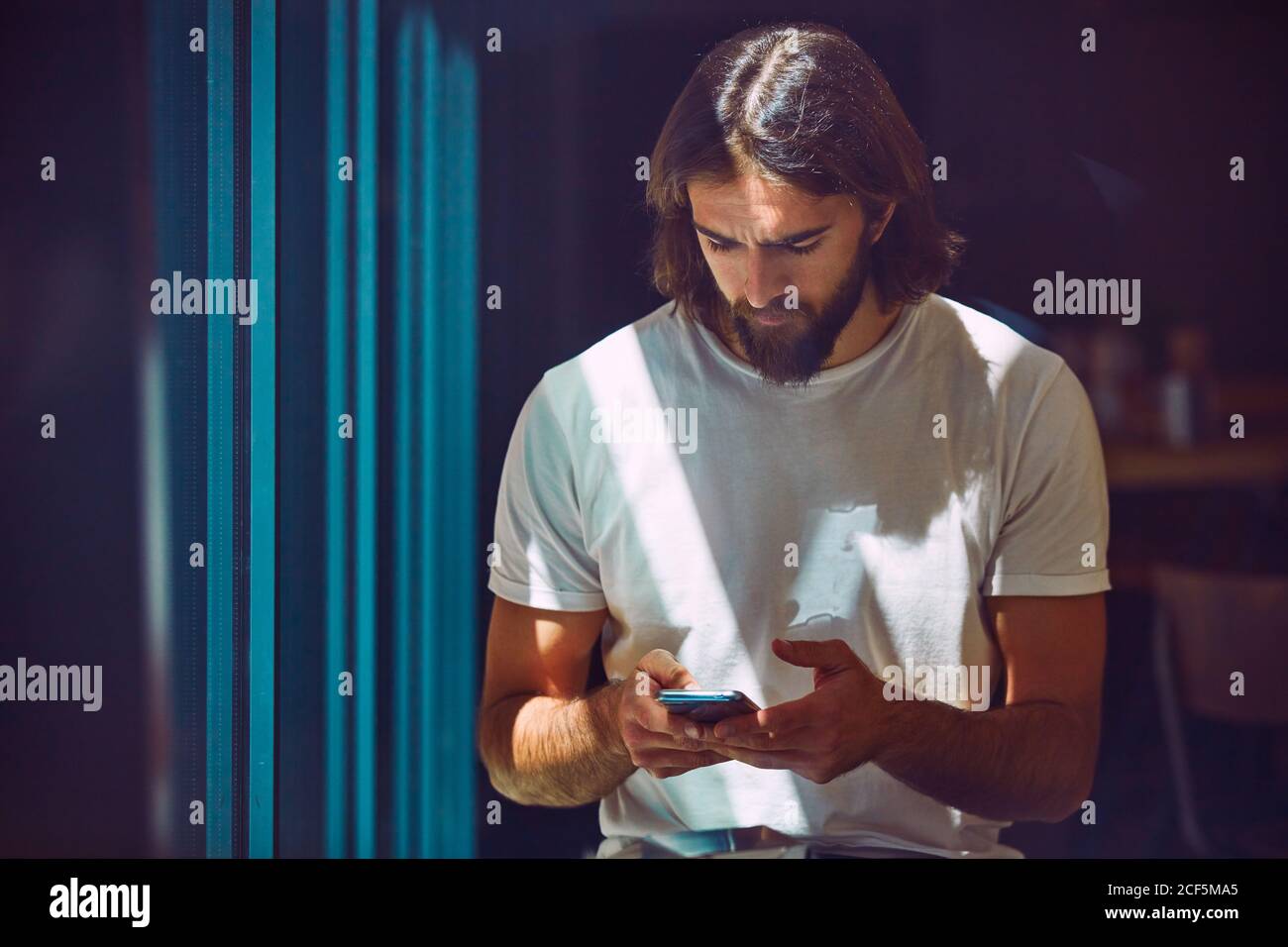 Jeune barbu beau homme penché sur le mur avec téléphone portable à vos mains, envoyez des sms avec soin Banque D'Images