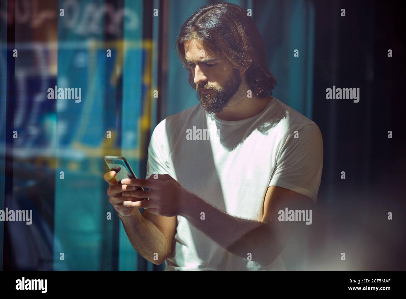 Jeune barbu beau homme penché sur le mur avec téléphone portable à vos mains, envoyez des sms avec soin Banque D'Images