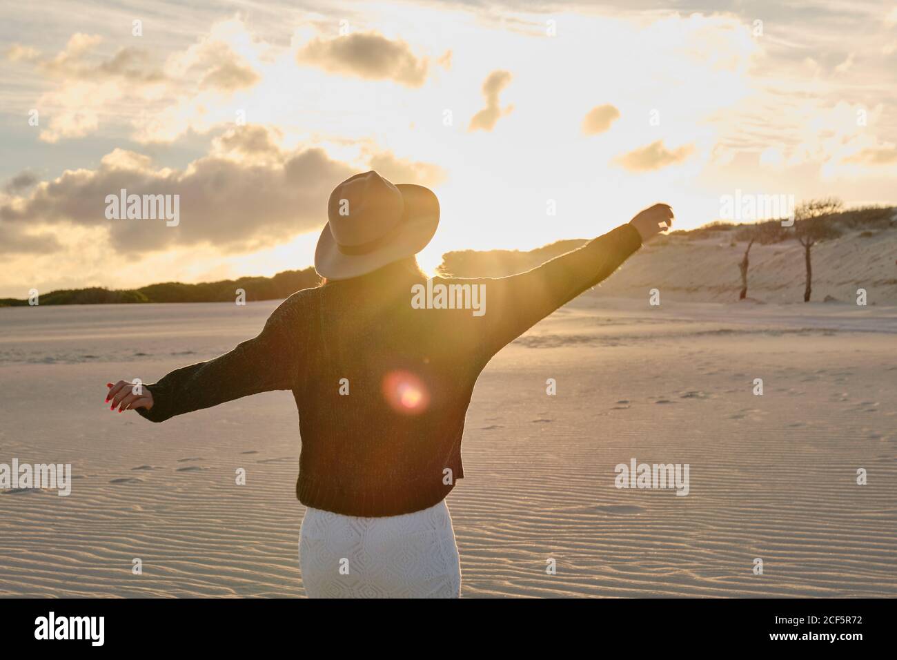 Vue arrière d'une femme de voyage méconnaissable en chapeau debout dans un désert de sable isolé au coucher du soleil à Tarifa, Espagne Banque D'Images