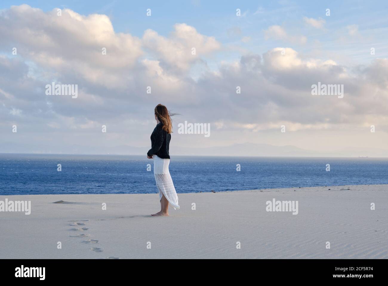 Vue latérale d'une femme se tenant dans un désert de sable isolé au coucher du soleil regardant la caméra à Tarifa, Espagne Banque D'Images
