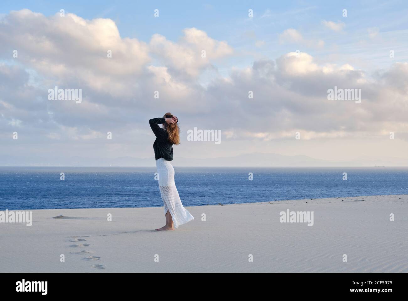 Vue latérale d'une femme se tenant dans un désert de sable isolé au coucher du soleil regardant la caméra à Tarifa, Espagne Banque D'Images